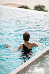 Naklejka premium Relaxing at swimming pool on rooftop, Woman enjoying the view with arms raised from swimming pool
