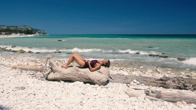 Slow motion: Woman relaxing on white gravel beach turquoise water Conero riviera coastline Italy travel destination sunny summer day