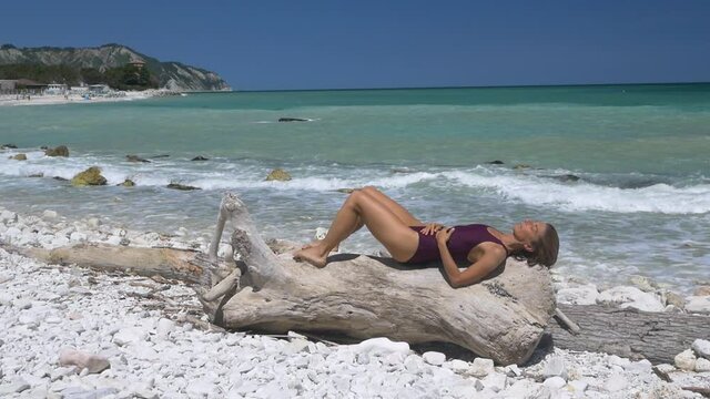 Slow motion: Woman relaxing on white gravel beach turquoise water Conero riviera coastline Italy travel destination sunny summer day