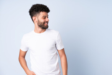 Young Moroccan man isolated on blue background having doubts while looking side