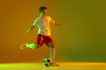 One male soccer football player in action and motion isolated on gradient green yellow background...