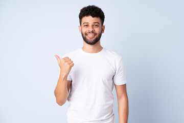 Young Moroccan man isolated on blue background pointing to the side to present a product