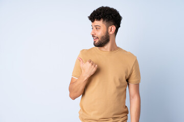 Young Moroccan man isolated on blue background pointing to the side to present a product