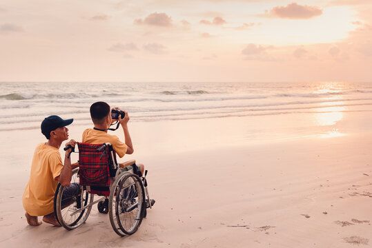 Asian special child on wheelchair on the beach with parents in family holiday to travel, Take photo the camera nature around the sea beach, Life in the education age, Happy disabled kid concept.