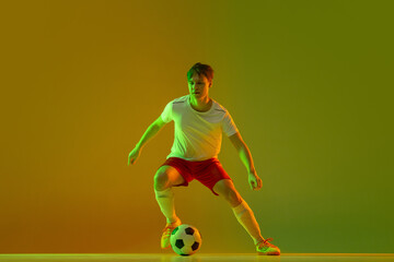 One male soccer football player in action and motion isolated on gradient green yellow background...
