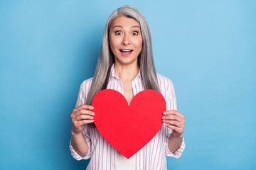 Portrait of attractive amazed cheerful woman holding in hands big large heart isolated over bright blue color background