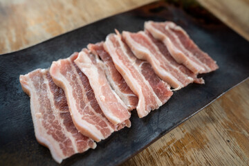 Sliced streaky pork served in black tray which is placed on the wooden table, Raw food for barbecue grill meal. 