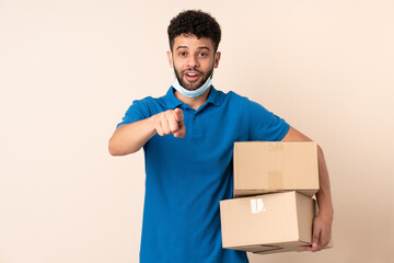 Young delivery Moroccan man isolated on beige background surprised and pointing front