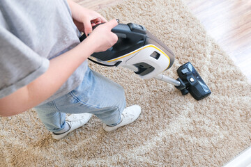 cordless vacuum cleaner is used to clean the carpet in the room. Housework with a new handheld vacuum cleaner. - obrazy, fototapety, plakaty