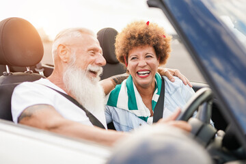 Mulitracial senior couple having fun inside convertible car - Mature people on a road trip in...
