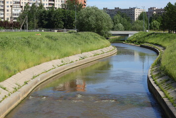 Fototapeta premium Narrow winding river with grass-covered banks in the city, Okkervil River, Rosiysky Prospekt, Saint Petersburg, Russia, June 2021