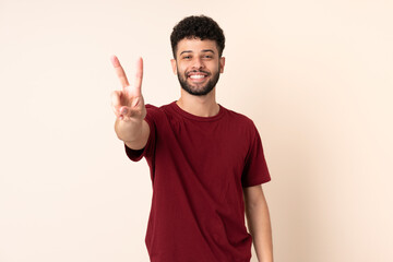 Fototapeta premium Young Moroccan man isolated on beige background smiling and showing victory sign