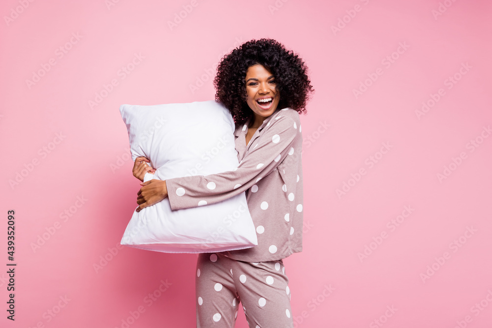 Poster Photo of sweet adorable wavy dark skin lady dotted sleepwear dancing hugging white pillow isolated pink color background