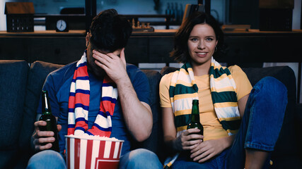 Fototapeta na wymiar man covering face near woman smiling and watching sport match at home.