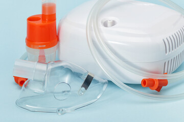 Respiratory mask, atomizing cup and compressor nebulizer on blue background. Medical equipment for...