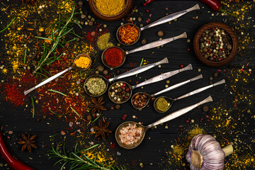 An assortment of oriental spices in iron spoons scattered on a black wooden surface as a background.