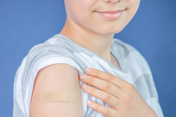 Teenage boy with adhesive bandage plaster on his arm after vaccination on blue background....