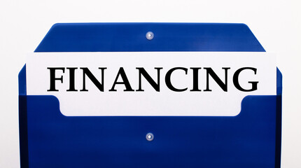 On a white background, a blue folder for papers. In the folder is a sheet of paper with the word FINANCING