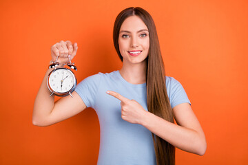 Photo of joyful young long hairdo lady point clock wear blue t-shirt isolated on orange color...