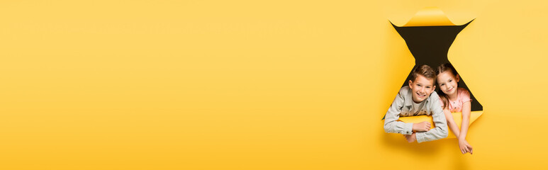 happy kids looking at camera through hole on yellow background, banner.