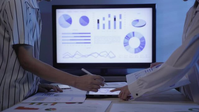 Business people working with diagram and chart at night. Two colleague overworked while brainstorm with document and graph for present of solution