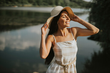 Fototapeta premium Relaxing young woman standing on wooden pier at the lake