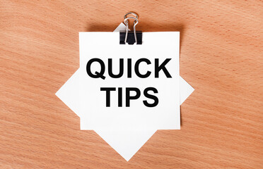 On a wooden table under a black paper clip lies a sheet of white paper with the text QUICK TIPS
