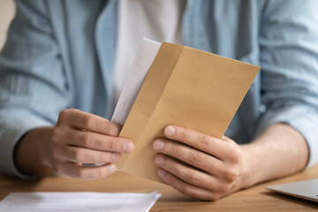 Close up young man opening envelope, feeling curious about getting paper correspondence. 30s male...