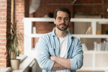 Portrait of confident young millennial generation businessman posing in modern office. Skilled professional handsome male manager worker employee teacher mentor in eyeglasses looking at camera