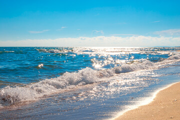 A blue sparkling sea with a wave rolling on the sand. Rest on the seashore