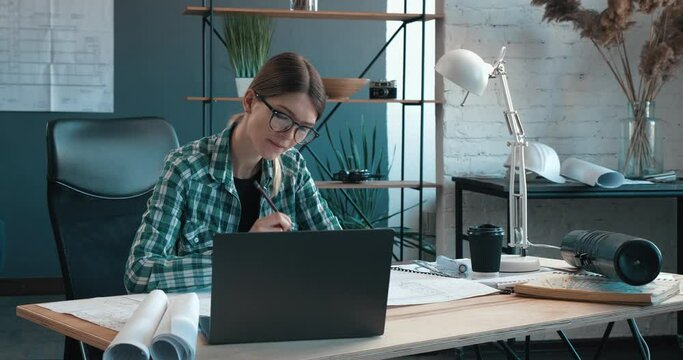 Female interior designer working in office with laptop. Architect thinks over architectural plan, searching new ideas for construction project. Woman sitting at workplace. Business portrait concept.