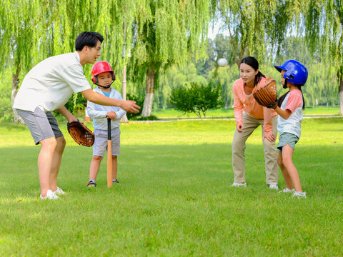 Happy family of four playing baseball in the park