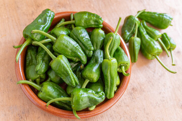 Padrón peppers in a clay container on a wooden background.
