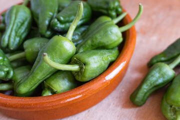 Padrón peppers in a clay container on a wooden background.