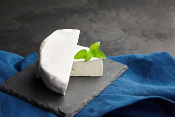 Camembert or brie cheese head on black slate board on blue linen napkin over dark background