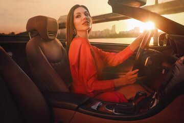 Sexy woman driving luxury convertible car at sunset - obrazy, fototapety, plakaty