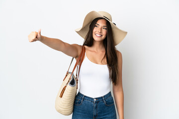 Young Brazilian woman with Pamela holding a beach bag isolated on white background giving a thumbs up gesture