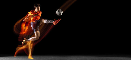 Young caucasian male football or soccer player kicking ball for the goal in mixed light on dark background. Concept of healthy lifestyle, professional sport, hobby.