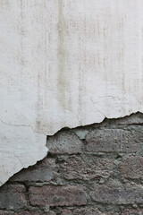 Obraz premium Wall with crumbling plaster. Traces of destruction. A brick wall. Poor-quality construction.A crack in the plaster.A wall with deep large cracks as a background or texture for the design.Vertical