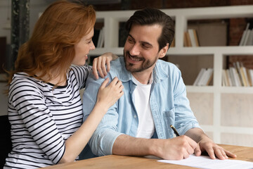 Happy bonding young family couple discussing offer, making common decision signing contract in...