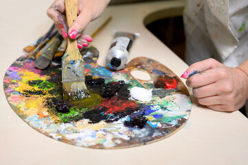 Creative female painter mixes palette of oil paints in palette. Close-up view. High quality photo