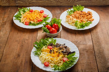 Three plates with different pasta on a wooden table near salted tomatoes.