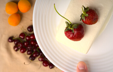 A large white ice cream is lying and strawberries are lying on a white plate in your hand.