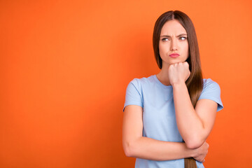 Photo of sad brown hairdo millennial lady hand chin look empty space wear blue t-shirt isolated on vivid orange color background