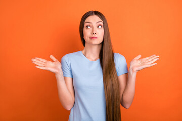 Photo of unsure brown hairdo young lady shrug shoulders look empty space wear blue t-shirt isolated on vivid orange color background