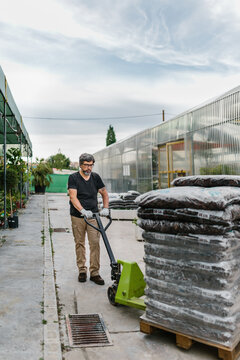 Mid adult man working in greenhouse. He is pulling a pallet