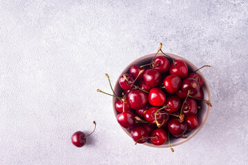 Cherries in a round white plate on gray plaster. Top view.