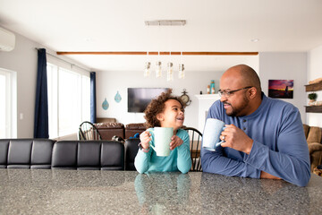 Laughing Father and daughter sit together at breakfast bar with drinks