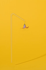 Creative concept of street light. Straw for juice and blue flower like a lantern. Isolated on a yellow background. 