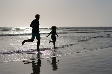 father and son silhouettes running having fun and feel freedom on summer beach, summer vacation